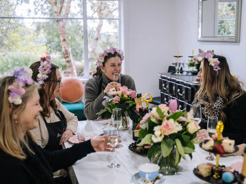 A group of people wearing flower crowns sat around a table smiling.